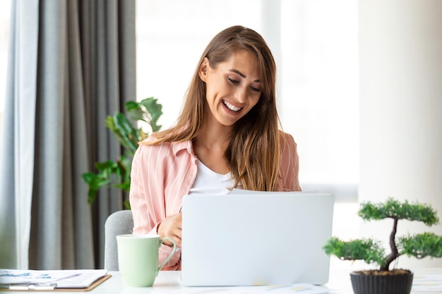 Focused business woman using laptop at home looking at screen\
chatting reading or writing email sitting on couch female student\
doing homework working on research project online