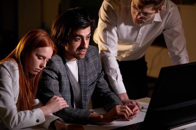 Focused Businessman Working With Sleepy Colleagues In Office At Night. Business Team Working On Computer, Discussing. Modern Loft. Working Overtime. Business Concept. Confident Businessman.