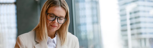 Focused businesswoman in glasses drinking coffee and making notes while working in cafe