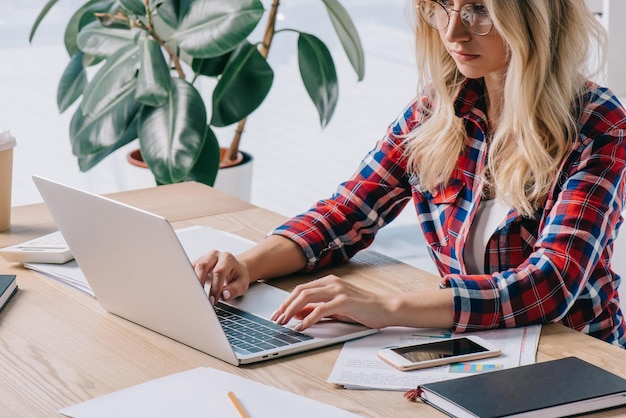 Focused businesswoman using laptop at workplace with papers