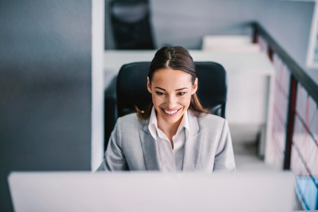 Focused businesswoman working at office and smiling at computer