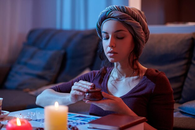 Focused calm soothsayer seated at the table holding a small ceramic container in her hands