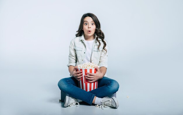 Focused child is sitting in a lotus position and eating popcorn, while watching cartoons or movies.