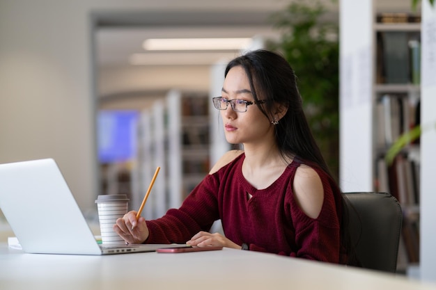 Focused chinese woman freelancer working remotely on laptop in public library or coworking
