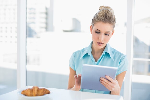 Focused classy woman using tablet while having breakfast