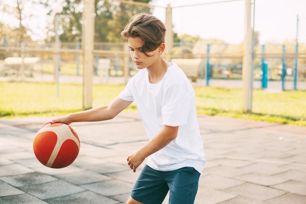集中した可愛い少年アスリートがバスケットボールの試合でボールをリードし少年が学校の後バスケットボールをします