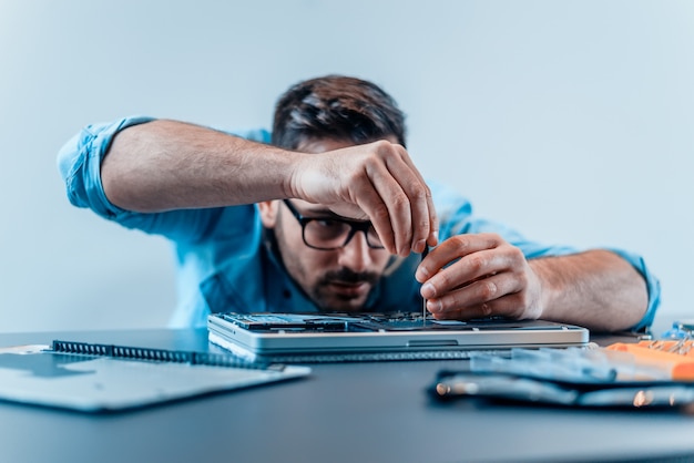 Focused engineer dismantling laptop with screwdriver.