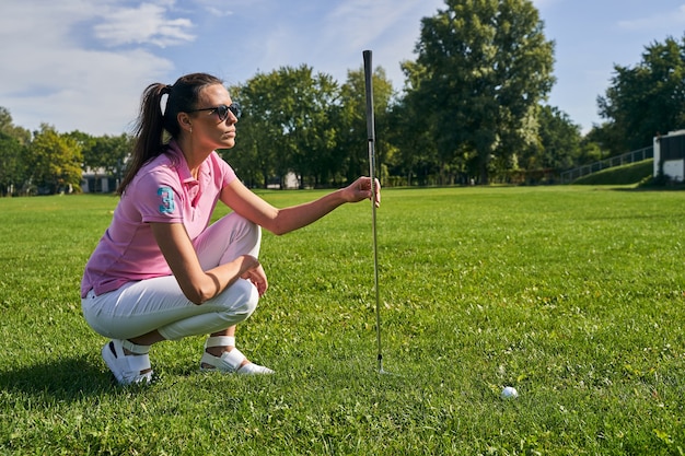 focused female golfer in sunglasses checking the ground on the course