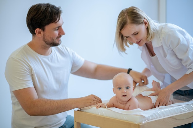 Focused female pediatrician examining a cute calm newborn child assisted by a young male parent