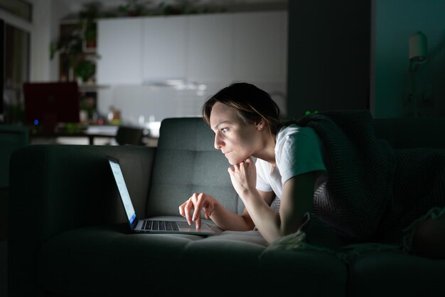 Focused female working online on laptop at home in the night looking at screen reading news media