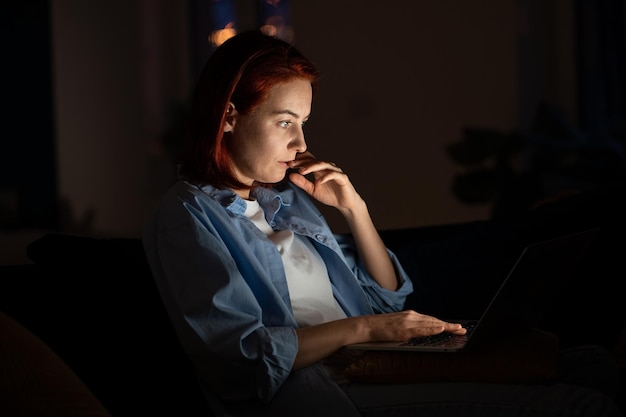 focused freelancer woman looking laptop screen at night working from home