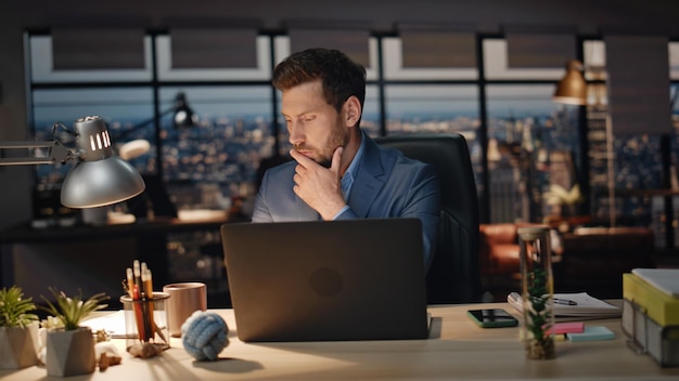 集中した男が暗い場所でお茶を飲んでいます近距離のオフィスワーカーがコンピューターを見ています