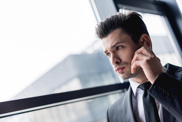 Focused handsome bodyguard in suit using earphone