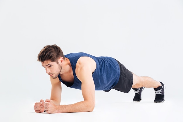 Focused handsome young sportsman doing plank core exercise over white background