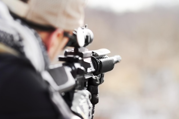 Photo focused on his target rearview of a snipper pointing his gun into the distance with copy space