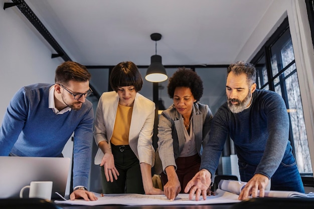 Focused interracial architects pointing at blueprints on a table on a meeting at boardroom