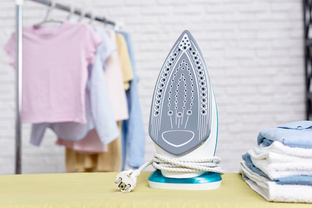 Photo focused iron near folded clothes and rack