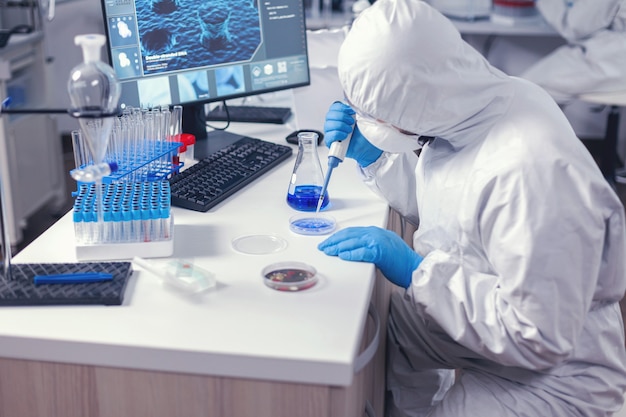 Сосредоточенный лаборант, дозирующий раствор в чашку Петри, работает на своем рабочем месте в современной лаборатории. Химик в современной лаборатории проводит исследования с помощью дозатора во время глобальной эпидемии covid-19.