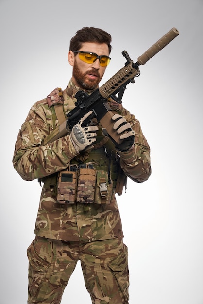 Сосредоточенный солдат в камуфляжном наряде перезаряжает снайперскую винтовку в помещении портрет кавказца