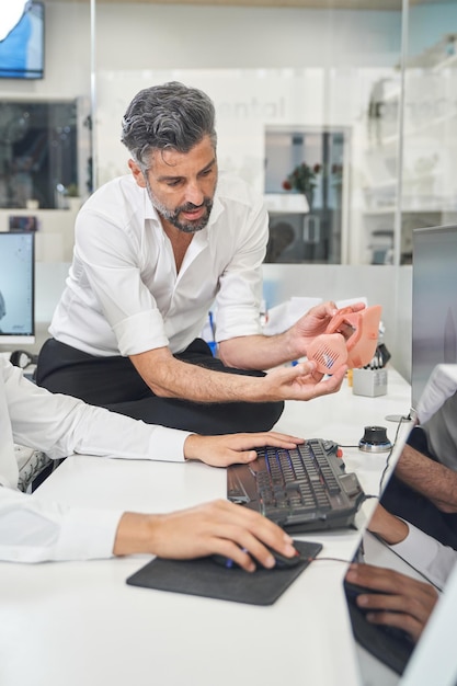 Focused male specialist with 3D printed respirator standing at table with computer near faceless colleague during work in modern laboratory