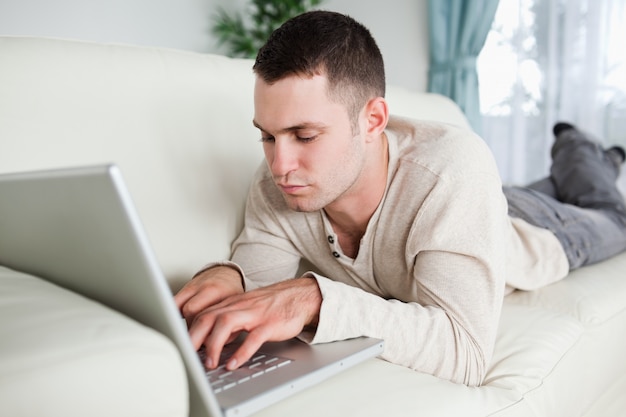 Focused man lying on a sofa using a laptop