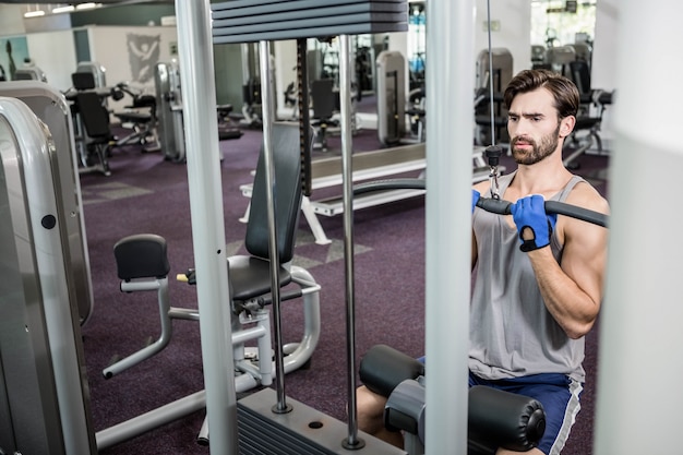 Focused man using weights machine for arms at the gym