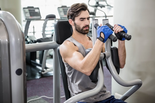 Uomo messo a fuoco usando la macchina dei pesi per le armi alla palestra