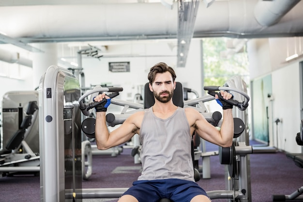 Uomo messo a fuoco usando la macchina dei pesi per le armi alla palestra