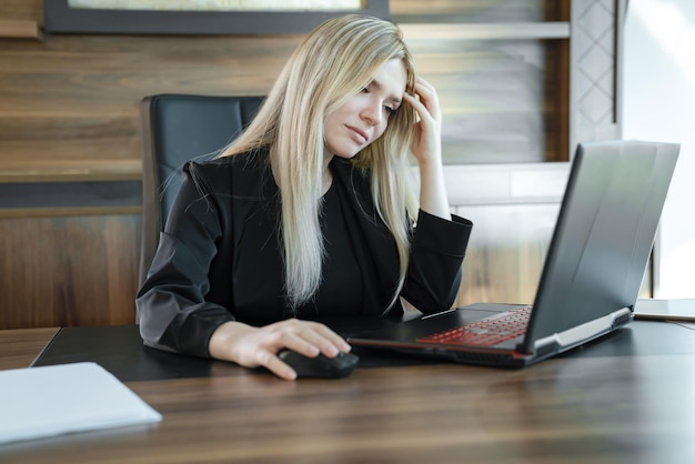 Focused meisje blonde in zwart pak zit voor de laptop in het kantoor concept van online onderwijs