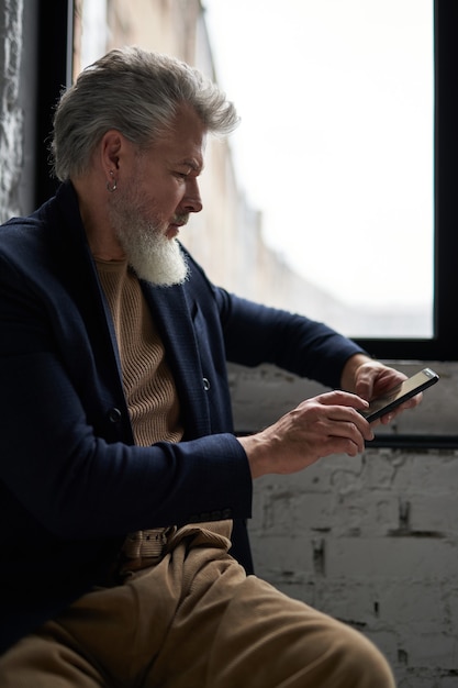 Focused middle aged man in business casual wear using his smartphone while sitting by a