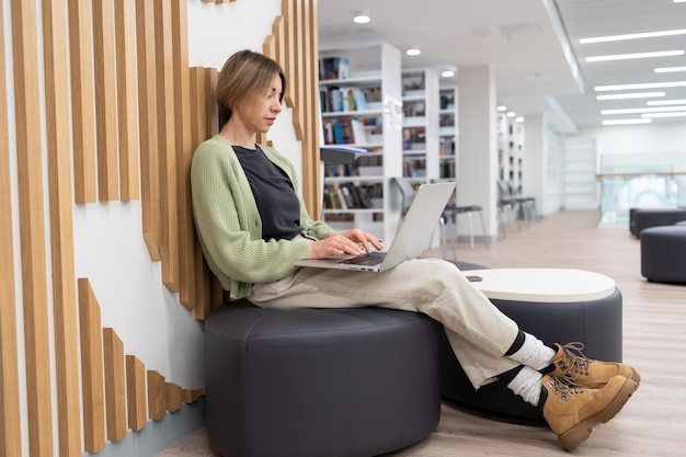 Foto donna di mezza età focalizzata freelance che lavora al computer portatile in libreria digitando sulla tastiera