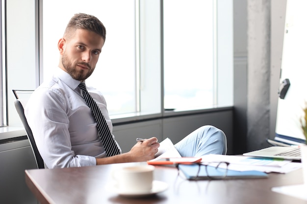 Focused modern businessman working and taking notes in his modern office.