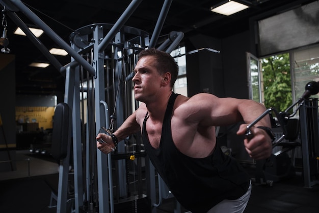 Focused muscular bodybuilder working out in crossover gym machine