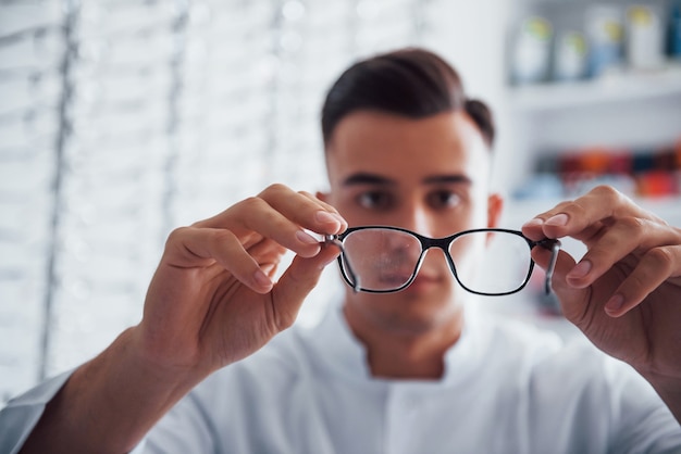 若い眼科医が室内で持っている真新しい眼鏡の焦点を合わせた写真。