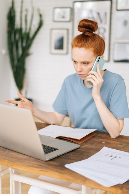 Focused redhead young woman accountant of corporation is making distant work