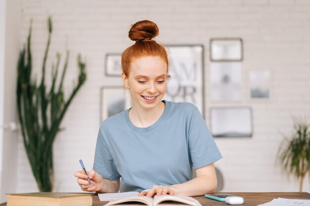 Focused redhead young woman is writing letter on table at home office