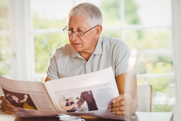 Focused senior man reading newspaper at home