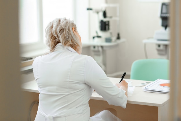 Focused short-haired doctor in white robe sitting at the table