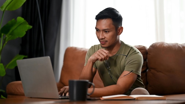 Focused and smart millennial Asian man looking at his laptop screen