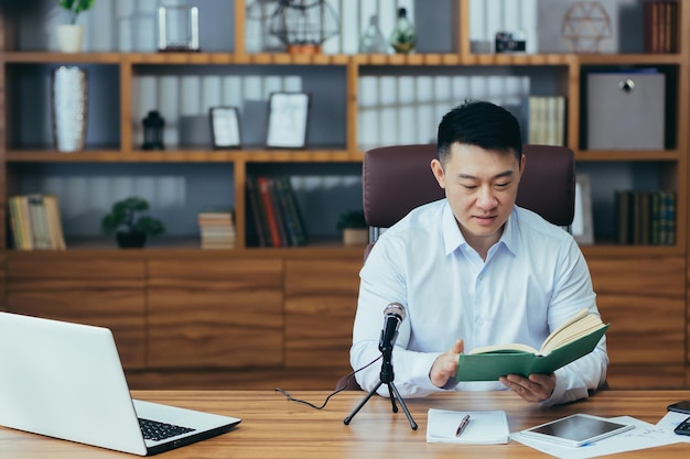 전문 마이크 녹음 오디오 팟캐스트 음성 연기 또는 스트리밍 교육 웨비나를 사용하여 집중적으로 웃고 있는 젊은 사업가가 노트북 화면을 바라보는 아시아인