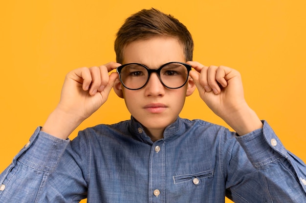 focused teenage boy in denim shirt adjusting his large black glasses