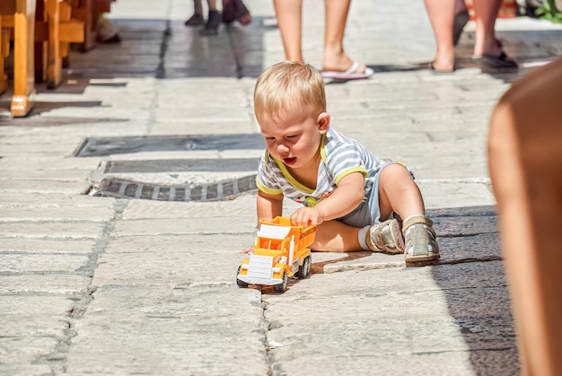 Focused toddler plays with truck toy near restaurant on narrow street in Omis
