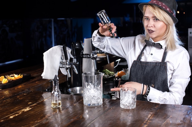 Focused woman bartender formulates a cocktail on the bar