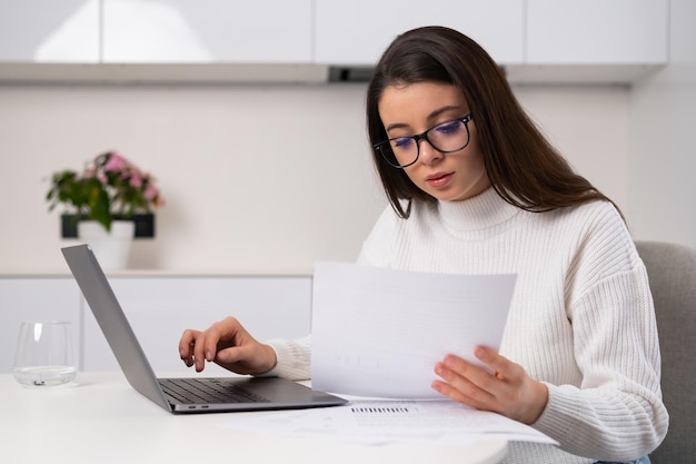 Focused woman enters data written in papers into Notebook