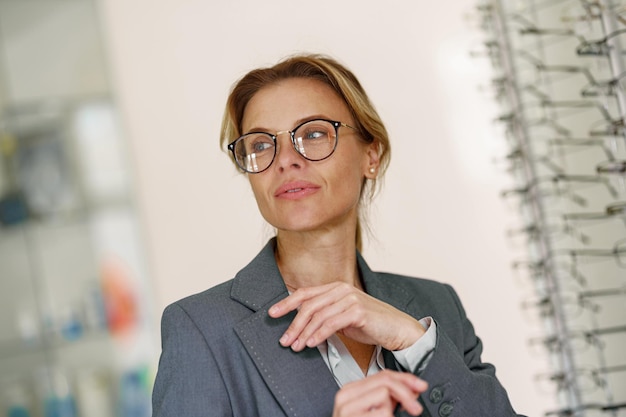 La donna concentrata con gli occhiali davanti alla vetrina in un negozio di ottica distoglie lo sguardo