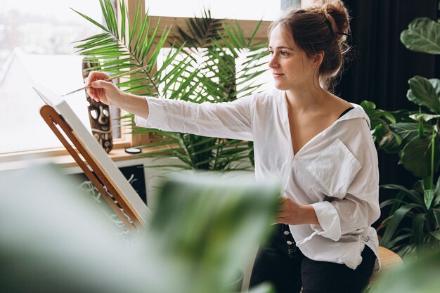 Focused woman painting with brush on easel