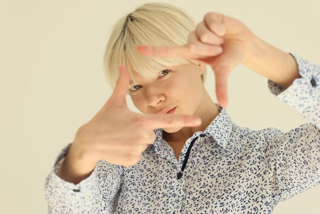 Focused woman puts fingers in shape of photo camera screen standing on beige background in