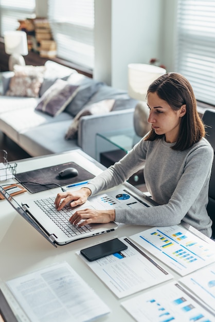 Focused woman working from home office on laptop.