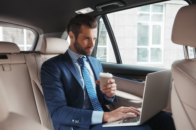 Focused on work busy young businessman in formal wear working on laptop and drinking hot