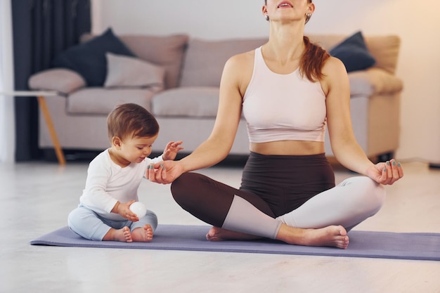 Focused at yoga exercises mother with her little daughter is at\
home together